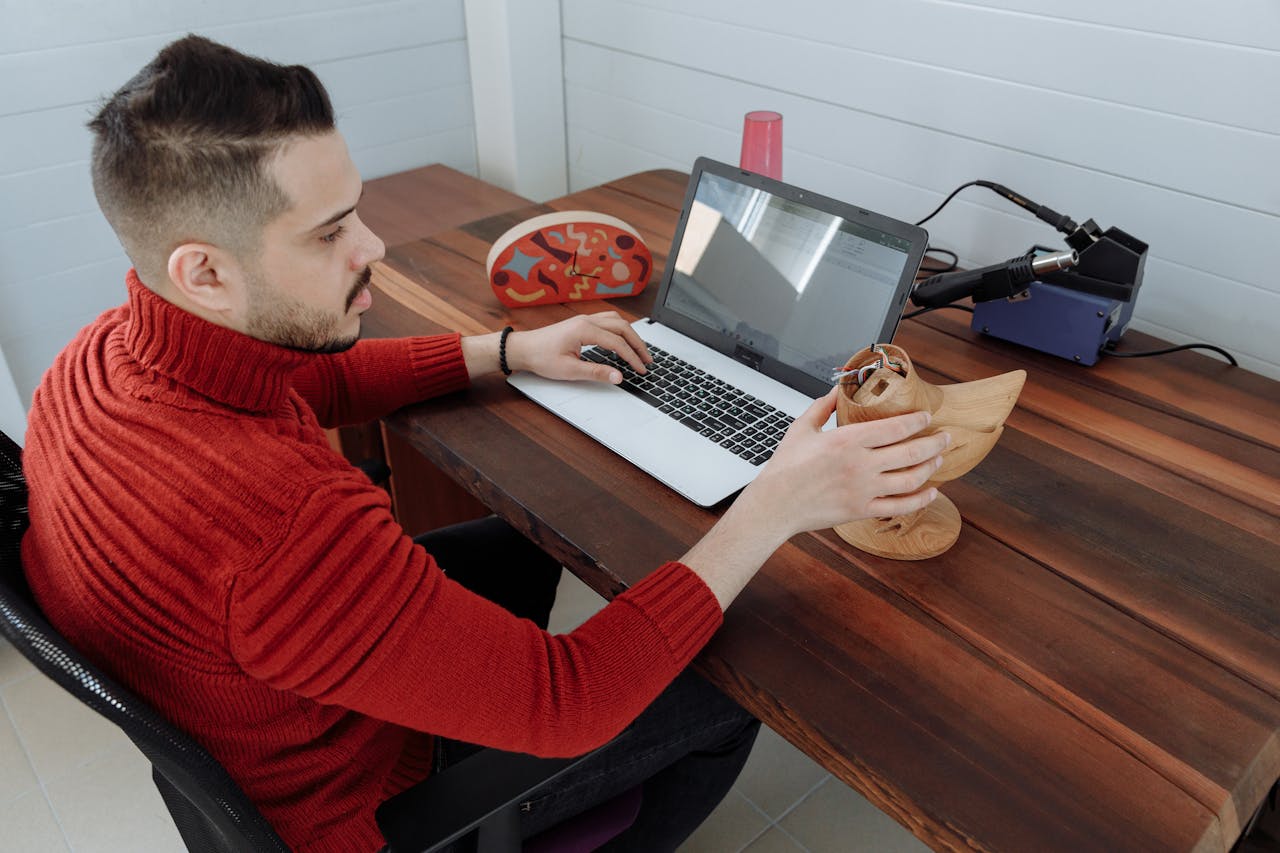 gallery-06 Engineer working on a laptop at a wooden desk, holding a 3D model in an office setting.